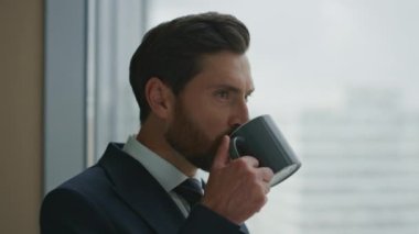 Başarılı sakallı yönetici ofiste kahve içiyor panoramik pencereye bakıyor şehir manzarasına yakından bakıyor. Çekici, kendine güvenen iş adamının portresi. Düşünceli patron rahatla..