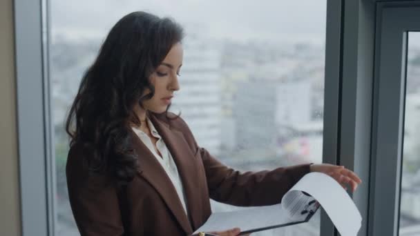 オフィスの窓に立っている仕事文書を読んでいるスマート女性の最高経営責任者 Ceo を閉じます ビジネス契約を探して魅力的な深刻なビジネス女性 会社の視点で考える取締役の心配 — ストック動画