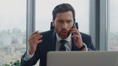 Kızgın CEO 'nun cep telefonu konuşmasında bağırması lüks ofiste otururken şık bir takım elbise giymesi. Kızgın yönetmen, mali sonuçtan memnun olmayan bir rapor aldı. İşçi stresli
