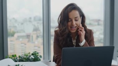 Başarılı gülümseyen iş kadını, ofis masasında dizüstü bilgisayarla telefon görüşmesi yapar. Zeki çekici bayan yönetici, telefon eden bilgisayar ekranını arıyor. Esmer kadın CEO konuşuyor..
