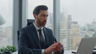 Yakışıklı sakallı yönetici, bilgisayardaki internet aramasını kullanarak ofis masasını kapatıyor. Kendine güvenen iş adamı el sallayarak video konferansını bitiriyor. Başarılı patron web kamerasında konuşuyor..