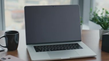 Modern, açık bir dizüstü bilgisayar ofis çalışma masasında işçi olmadan duruyor. Bilgisayarı kapatılmış ahşap masa, kahve fincanı, cep telefonu saksısı. İş yazılımı teknolojisi kavramı.