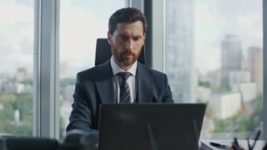 Bilgisayarla modern ofiste çalışan odaklanmış sakallı bir iş adamının portresi. Bilgisayar klavyesinde yazı yazan çok çekici bir yönetici. Monitöre yakından bakıyor. Şirket sorunlarını çözmek için yetenekli bir işçi.