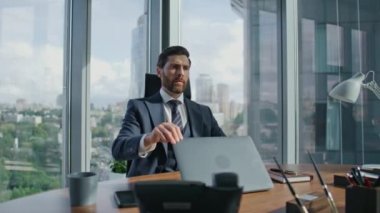 Odaklanmış yönetici, ofis masasında şık bir takım elbiseyle dizüstü bilgisayarını kapatıyor. Güvenilir sakallı iş adamı şirket işlerini dert ediyor. Düşünceli yönetici, bilgisayar kapağını kapatıyor ve iş başarısızlığını düşünüyor.