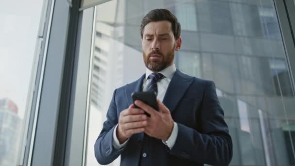 深刻な髭の会社の経営者は 近代的なオフィスの近くに立って満足していない電話 重要な会議を待っている時計を見てスマートフォンを保持する神経質なビジネスマン 起業家 — ストック動画