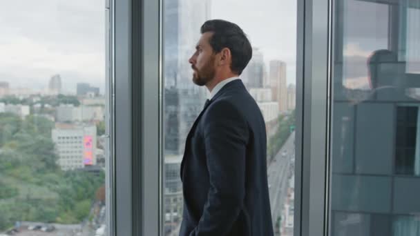 沉思的金融家穿着雅致的西服站在办公室窗前 有自信的大胡子商人认为公司的发展对事业的发展大有裨益 男经理在等会议 — 图库视频影像