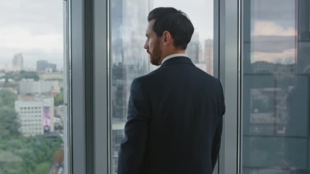 高瞻远瞩的公司员工站在办公室窗前 凝视着美丽的城市风景 创造出了商业策略 有魅力的大胡子商人 穿着时髦西装 思考职业前景 — 图库视频影像