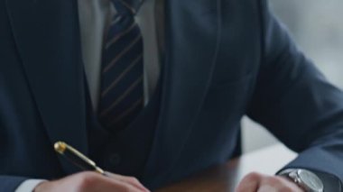 Ofis masasında oturan kendine güvenen ticari direktör, ortaklık anlaşmasıyla kağıtları imzalıyor. Sakallı yönetici finansal belgeleri imzalıyor. Yönetici sözleşmeyi sonlandırıyor.