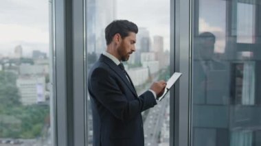Ofis penceresinde duran tablet üzerinde çalışan ciddi sakallı girişimci. Bilgisayardaki bilgilere bakan kendine güvenen akıllı finansörün yan görüntüsü. Düşünceli iş adamı düşünme sorunu.