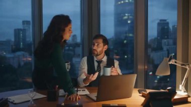 İki iş arkadaşı gece geç saatlerde ofis masasında kahve içmekle meşguller. Modern işyerinde iş meselelerini birlikte çözmeye odaklanmış ortaklar. Çok çalışan iş arkadaşları kahve molasının tadını çıkarır.