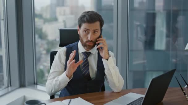 聪明的大胡子企业家在笔记本电脑上工作时讲智能手机 有信心的认真的商人坐在办公室的办公桌前进行电话商谈 Ceo经理在手机通话时在笔记本上留言 — 图库视频影像