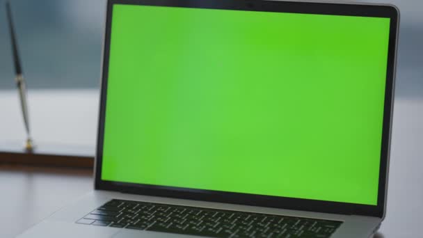オフィスの机の上に置かれた近代的な緑のスクリーンノートパソコンを閉じます 会社の仕事の準備ができてモックアップノートブックモニターをオンに表示されます 職場での空の緑の画面のクロマキーコンピュータディスプレイ — ストック動画