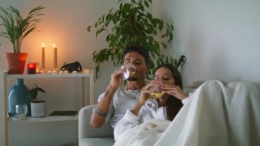 Gülen çift evde şampanya test ediyor. Neşeli adam ve kadın oturma odasında beyaz şarap içiyorlar. Mutlu bir çift gözlüklü kanepe. Genç aile otelde yıldönümünü kutluyor.