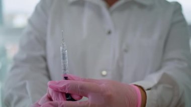 Kimliği belirsiz güzellik uzmanı elinde hiyalüronik asitle şırınga tutuyor. Kadın elleri pembe eldivenlerle cilt tazeleme için ilaç hazırlıyor. Kozmetoloji kliniğinde güzellik prosedürü.