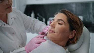 Çekici bir kadın, yalancı sandalye modern kozmetoloji kliniğini kapatıyor. Zarif bayan cilt yenileme için kaldırma işlemi yapıyor. Profesyonel güzellik uzmanı kolajenle şırınga kullanıyor.