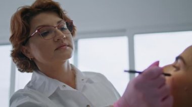 Orta yaşlı kadın estetik cerrah müşterinin yüzünü yaşlanma karşıtı ameliyata hazırlıyor. Deri tedavisinden önce modern klinikten gözlüklü deneyimli bir güzellik uzmanı düzeltme çizgisi çiziyor..