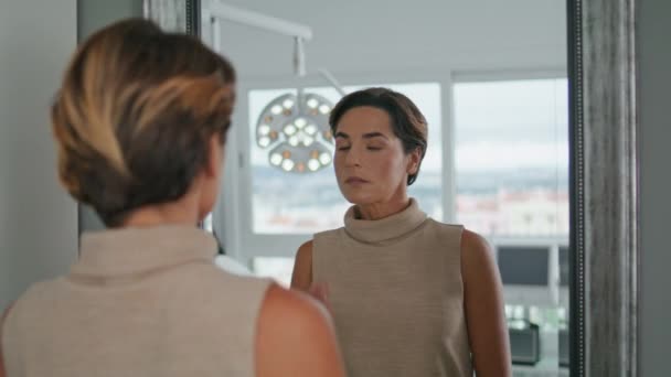 Medelålders Kvinna Tittar Spegel Stående Modern Kosmetologi Klinik Nära Håll — Stockvideo