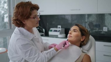Profesyonel güzellik uzmanı beyaz kalemle kadın yüzüne düzeltme çizgileri çiziyor. Prosedürü gençleştirme konusunda uzman. Estetik kozmetik uzmanı yüz derisindeki sorun bölgelerini işaretliyor.