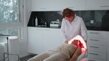 Profesyonel kozmetik uzmanı, yalan söyleyen bir kadın için lamba tedavisi yapıyor. Sertifikalı güzellik uzmanları ışıkla fotodinamik terapi için ekipman ayarlıyorlar. Modern güzellik salonu cilt bakımı.