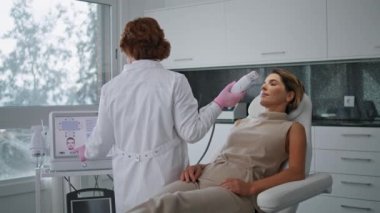 Doktor, kozmetoloji ekipmanlarını ultrason yüz tedavisine ayarlıyor. Kadın müşteri cilt bakımı için estetik uzmanı ekipmanı hazırlıyor. Modern güzellik kliniğinde cerrahi olmayan gençleştirme.