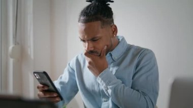 Arka planda cep telefonu kullanan sinirli bir adam. Sinirli adam akıllı telefon ekranı gibi görünüyor. Stresli yakın çekim. Afrika kökenli Amerikalı çağdaş insan cep telefonundan mesaj okuyor. Çalışma sorunları 