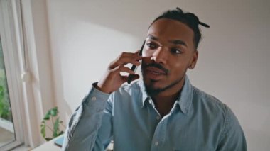 Uzaktan kumandalı iş yerinde gülümseyen adam akıllı telefondan konuşuyor. Afrika kökenli Amerikalı profesyonel ofis telefonuyla konuşuyor. Neşeli yönetmen iç mekândaki telefonu arıyor. Meslek kavramı 