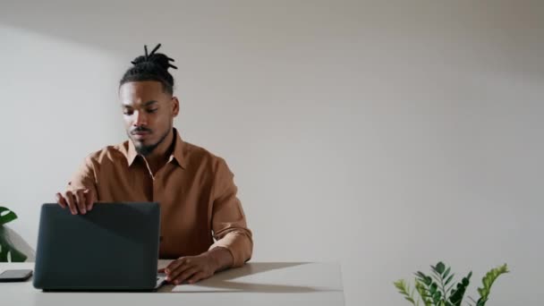 自宅のクローズアップで深刻な男のラップトップを開きます 若い男がロフトのインテリアで働き始めた アフリカ系アメリカ人のフリーランスは テーブルの職場だけでキーボードを入力します 屋内でコンピュータを使用するスマート学生 — ストック動画