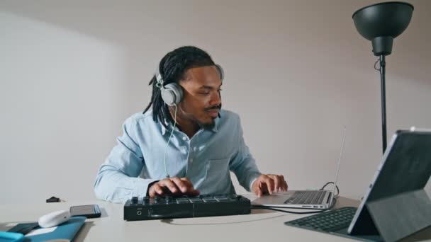 耳机男使用控制器公寓特写 非裔美国人音乐制作人摸Midi键盘看笔记本电脑 认真安排在家庭录音室创作歌曲的音响设备的工作 — 图库视频影像