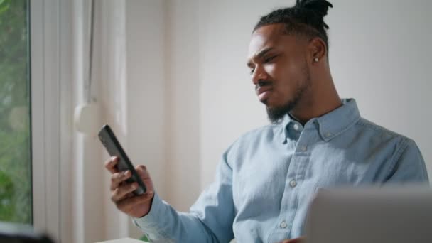 沮丧的男人看手机在家里的办公室特写 忧心忡忡的商人在手机上查看坏消息 非洲裔美国人在公寓里收到负面邮件很难过 自由的概念 — 图库视频影像