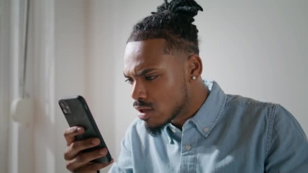 忧心忡忡的商人看着手机在家里的办公室特写镜头 沮丧的黑头发男人在手机上看坏消息 一个心烦意乱的非洲裔美国人收到负面邮件时感到很难过 自由的概念 — 图库视频影像