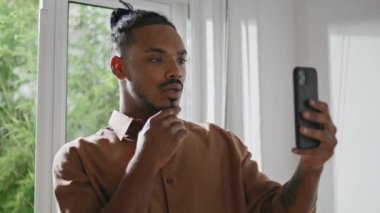 Modern adam akıllı telefon görüşmesini yakından açıklıyor. Afro genç adam cep telefonu kullanarak sanal sohbet yapıyor. Çağdaş serbest yazar görünümlü ekran, beyaz iç mekan arkadaşı ile çevrimiçi konferans yapıyor 