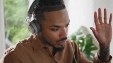 Kulaklık öğrencisi, video görüşmesini evde tamamlıyor. Çevrimiçi konuşan serbest çalışan. Genç afro adam öğretmeniyle sanal görüşme yapıyor. Modern ciddi adam iç mekanda bilgisayardan konuşuyor.