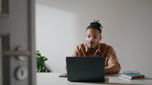 ノートパソコンのホームクローズアップを説明するフレンドリーなフリーランス アフリカ系アメリカ人の男がビデオチャットでビジネスパートナーと話してる 国内の職場でオンライン会議を話すビジネスマンをジェスチャー — ストック動画