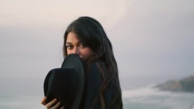 Playful attractive woman posing at dusk seashore close up. Smiling brunette looking camera standing in front gray dramatic seascape. Beautiful young model enjoy calm evening time on nature alone.