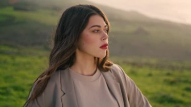 Portrait of seductive beautiful model posing on nature autumn day. Confident young woman with red lips looking camera standing valley green grass alone close up. Attractive girl enjoying landscape.