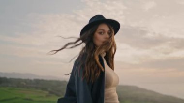 Active energetic girl wanderer walking green valley wearing stylish hat close up. Dark-haired attractive woman going on beautiful autumn nature alone. Pretty relaxed model enjoying weekend leisure.