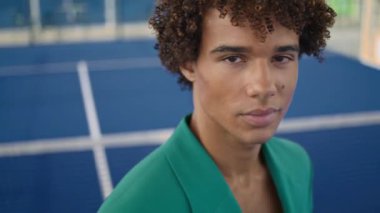 Curly teenager looking lens at stadium background portrait. Serious model posing alone in fashion clothes. Stylish hair guy showing individuality closeup. Young man face relaxing outdoors at summer