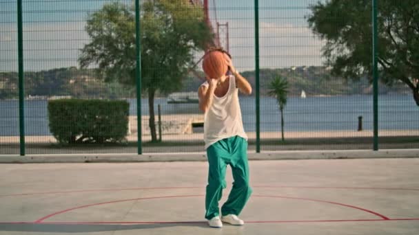 卷曲的家伙在运动场上打篮球 聪明的少年在阳光灿烂的早上体育馆把球丢进篮筐里 认真提高学生在城市操场上的技能 在街上锻炼的年轻人 — 图库视频影像
