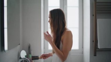 Focused woman combing hair at mirror place close up. Confident model making hairstyle in bath room alone. Gorgeous girl doing everyday morning routine at modern apartment. Daily beauty procedures