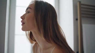 Smiling lady looking mirror at bathroom closeup. Stunning woman tucks hair behind ear feeling satisfied alone. Young model doing beauty routine at light modern apartment. Female health concept