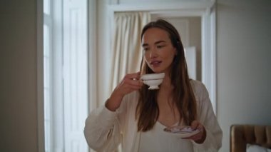 Romantic model drinking cappuccino at morning interior closeup. Relaxed woman holding coffee cup walking alone at living room. Positive girl looking window enjoying aromatic beverage at cozy apartment