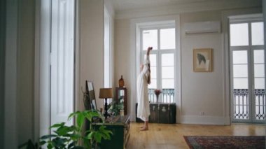 Stretching woman watching window at morning room. Relaxed girl in silk nightgown started day at home interior. Calm lady standing alone enjoying lazy weekend at cozy apartment. Domestic lifestyle