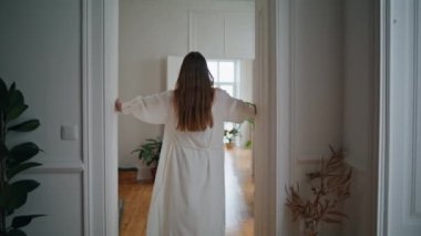 Young lady opening doors at morning interior. Unknown woman greeting new day crossing light apartment. Relaxed girl walking at cozy home back view. Calm female person in nightgown spending time alone