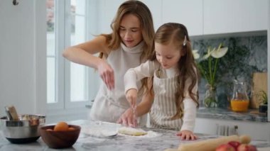 Cheerful woman pouring flour on table indoors closeup. Sweet family preparing food together. Mother and daughter time in kitchen room. Mom and child making biscuit at home. Homemade cuisine concept