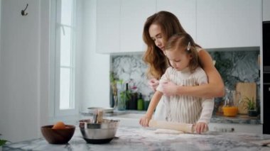 Caring mother rolling sleeves to daughter at kitchen closeup. Mom teaching child preparing dough on table. Cute kid helping parent with cake. Single woman and little girl cooking together at home
