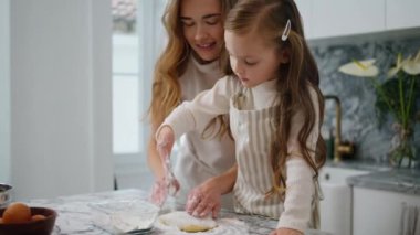 Curious kid sprinkling flour on table closeup. Single mother teach daughter bake in kitchen. Friendly family cooking cake. Loving woman and baby girl spending time together enjoying domestic routine