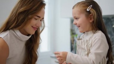 Cute kid touching mother face at kitchen portrait. Laughing woman bonding to daughter indoors close up. Funny baby enjoying time with mom cooking in home interior. Lovely family having fun together
