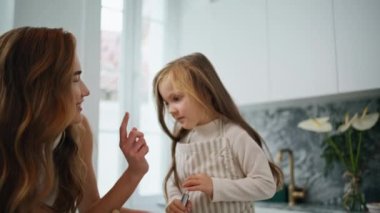 Laughing mother touching daughter nose at kitchen close up. Attractive woman and girl preparing dough cooking in modern home interior. Cute family having fun spending time together at light apartment