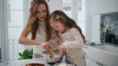 Caring woman talking child at kitchen close up. Positive family creating dough together at domestic place. Smiling mother mixing whisk spending time with daughter. Mommy teaching lovely kid to cook