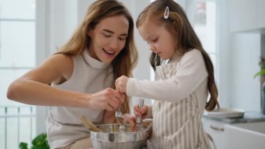 Mom daughter whisking dough indoors closeup. Overjoyed woman little girl making holiday cake at kitchen. Adorable child helping lady cooking. Mother kid baking pastry mixing flour to recipe together